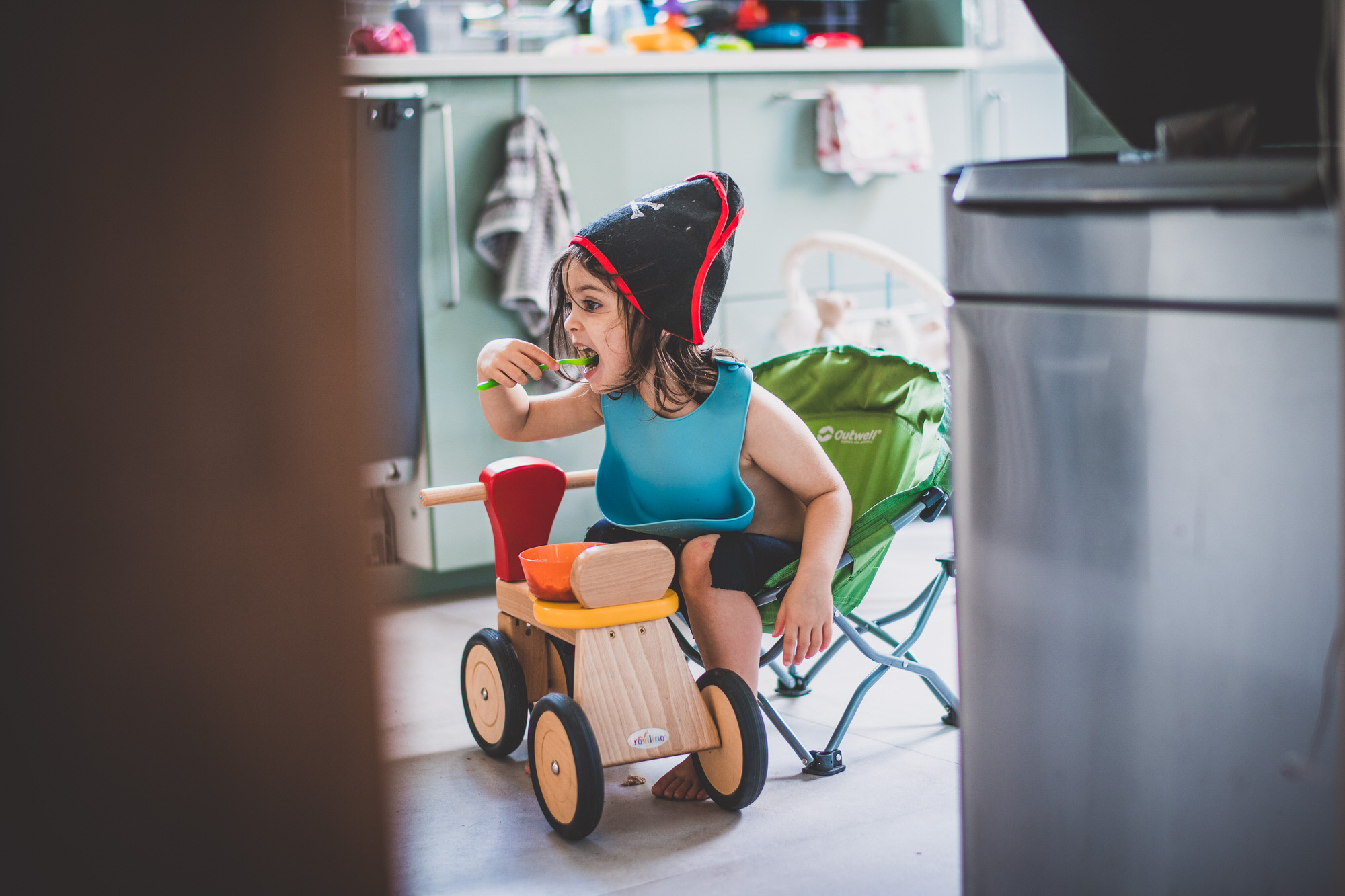 A child is sitting on a wooden toy in a kitchen, while the groom captures the moment as a wedding photographer.