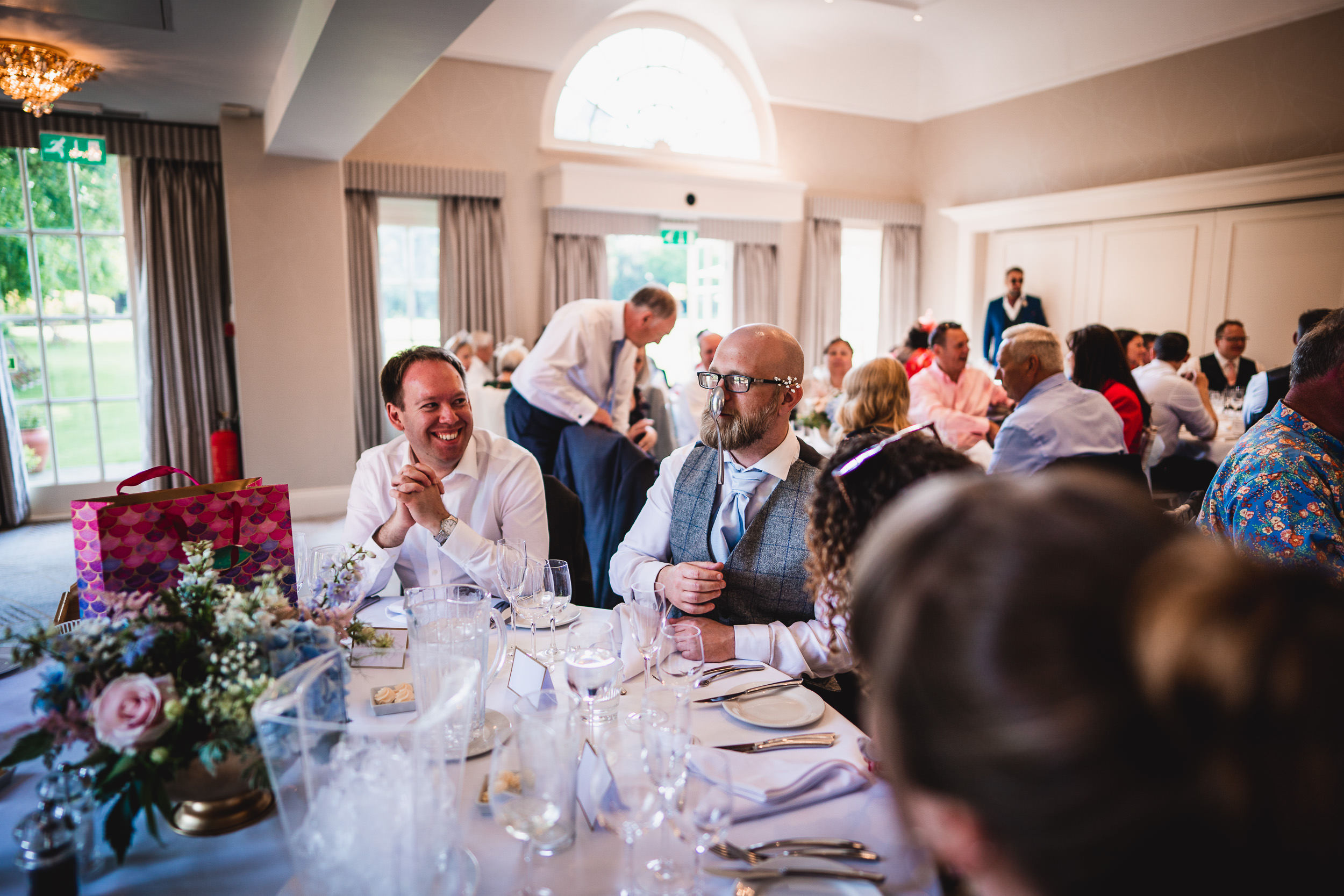 People seated around a table at a formal indoor event. The table is set with glasses, plates, and floral arrangements.