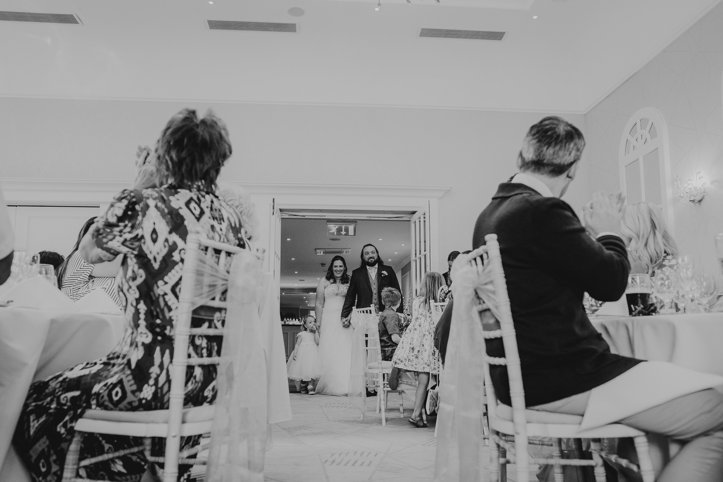 A couple in wedding attire enters a room as seated guests applaud.