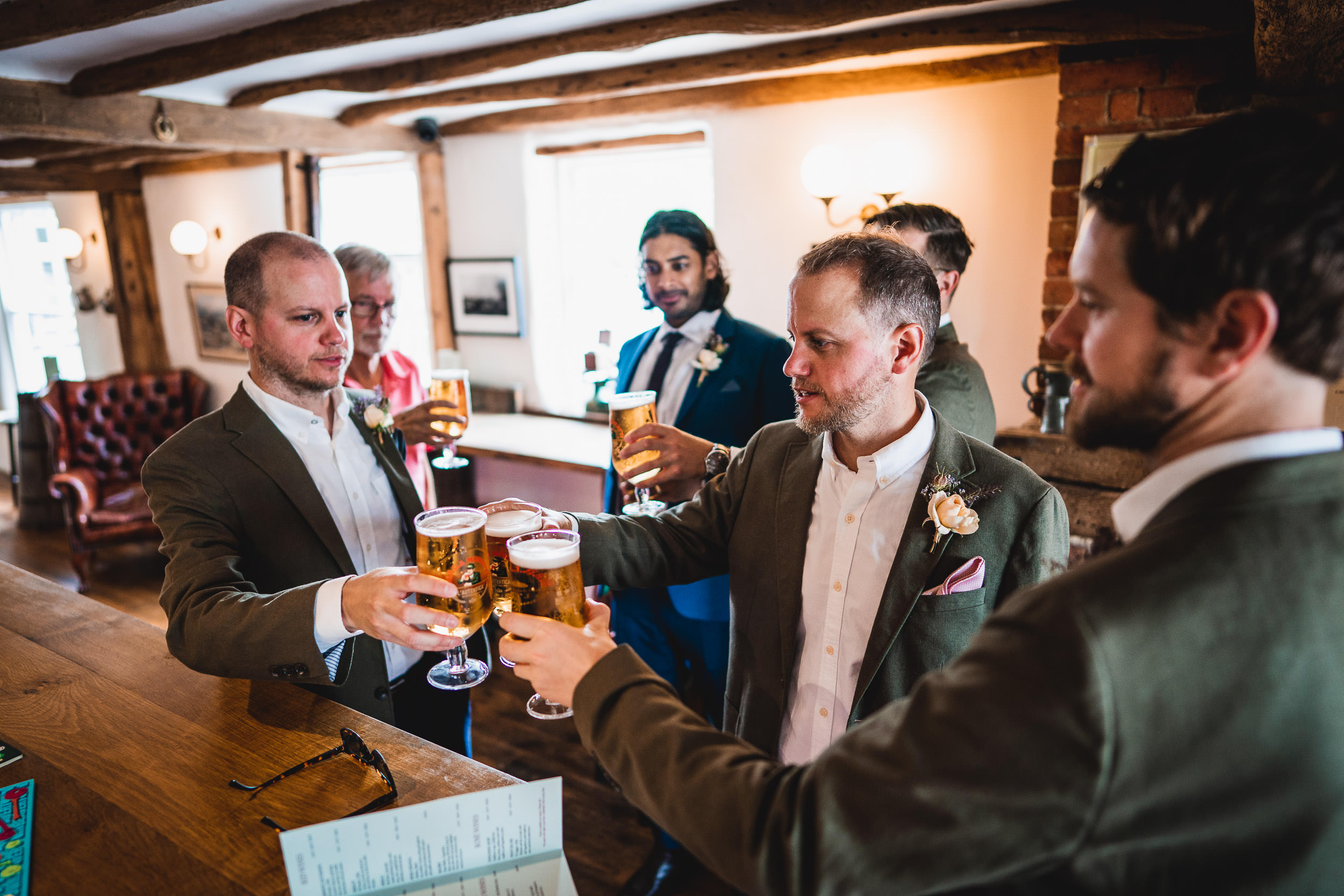 A group of men in suits toasting with beers at a bar inside a warmly lit room.