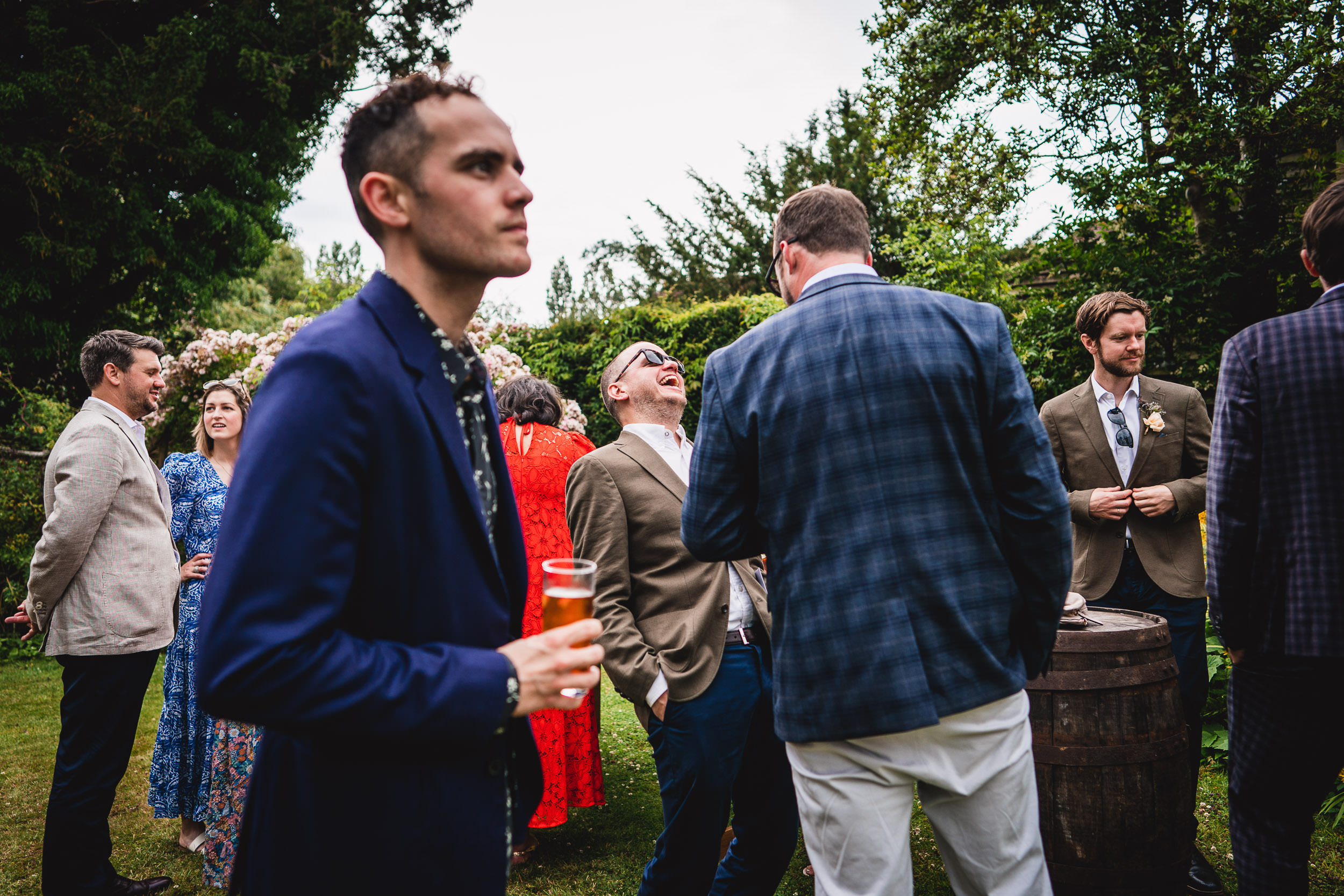 A group of people in formal attire stand and converse outdoors. One person is holding a drink.