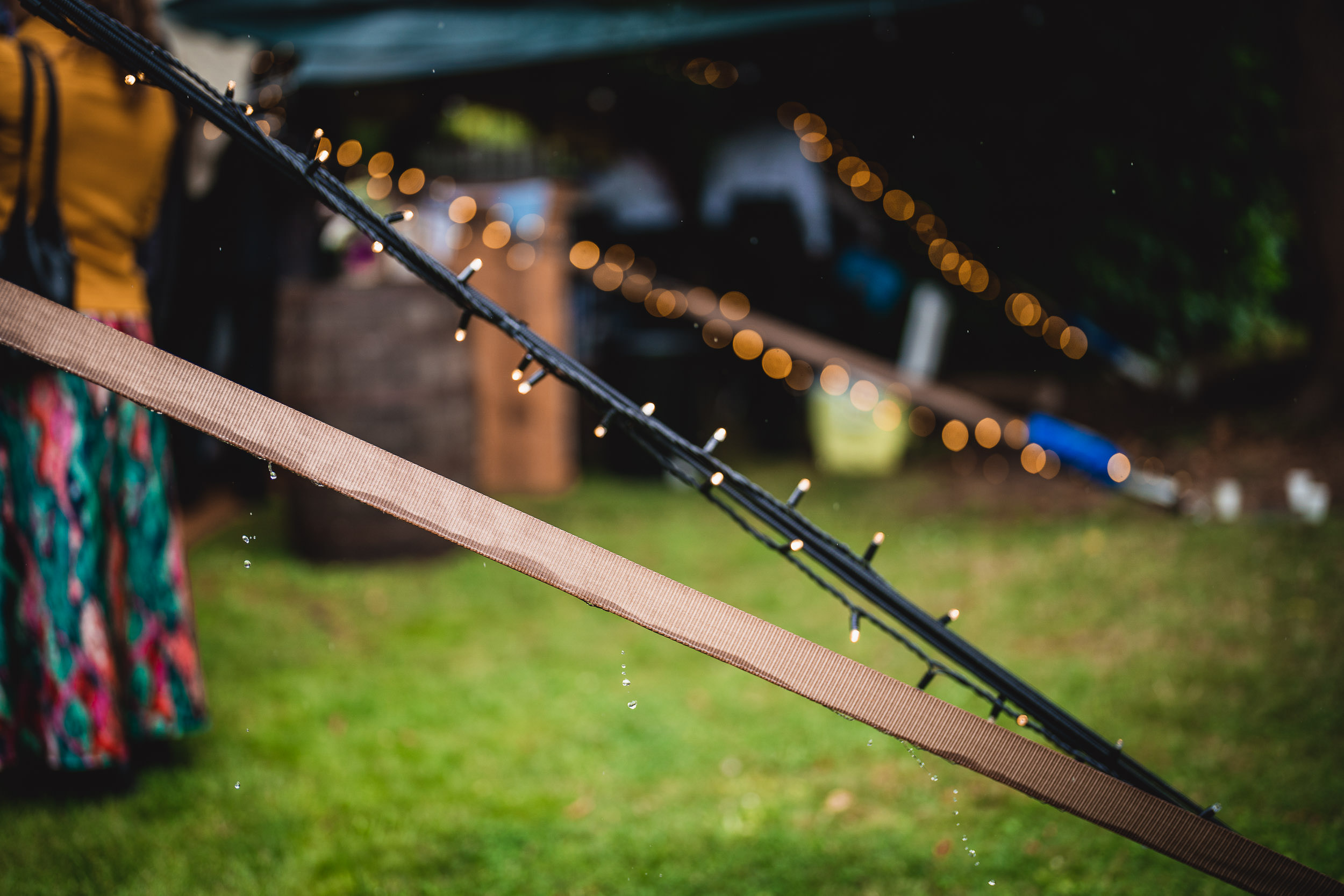 Close-up of decorative string lights and a wooden beam with blurred outdoor event in the background.