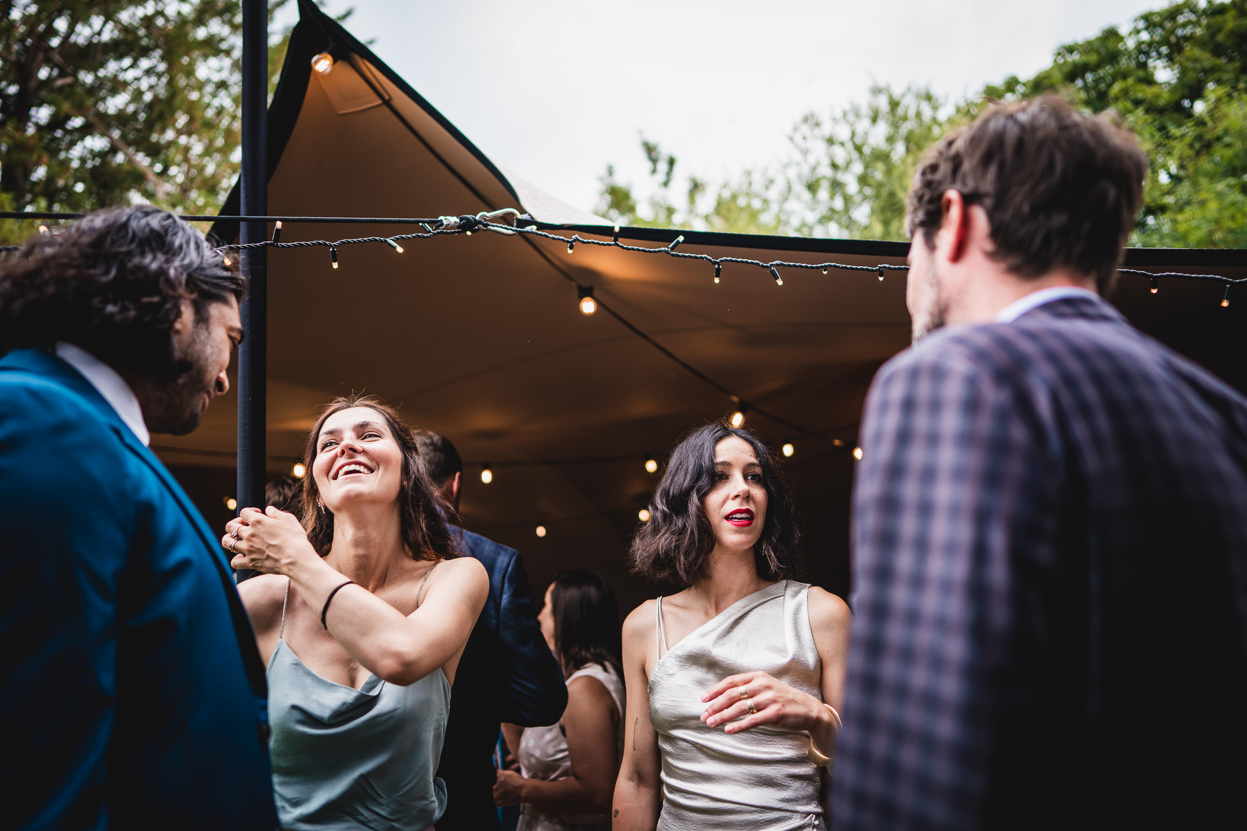 People in formal attire socializing outdoors under string lights near a tent.