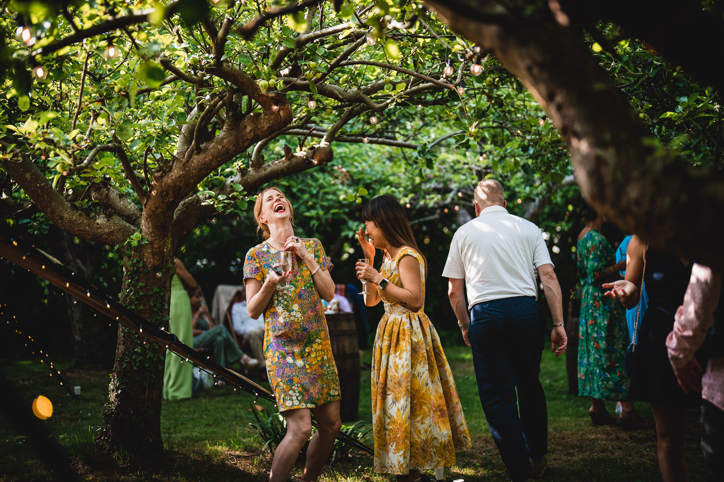 A group of people in colorful summer outfits enjoying a lively outdoor gathering under leafy trees.