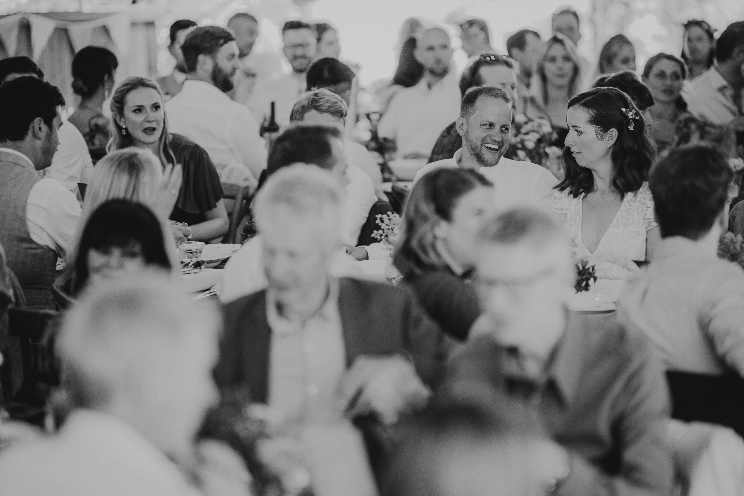 A black-and-white photo of people seated at a busy event, engaging in conversation and dining.