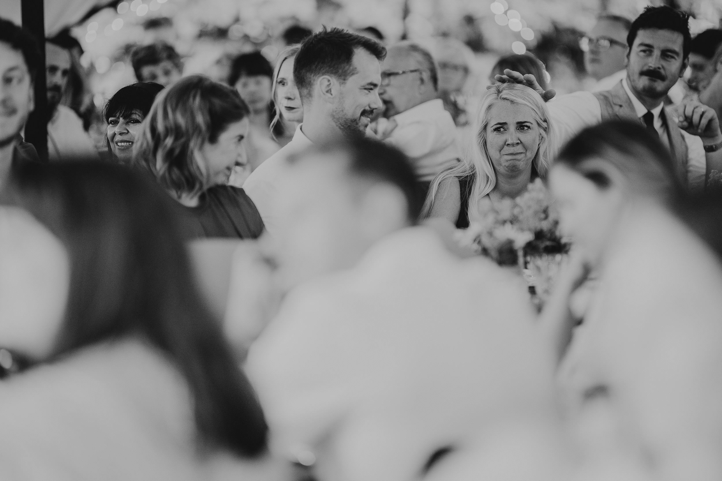 A black and white photo of a group of people seated closely together, some engaged in conversation at an event or gathering.