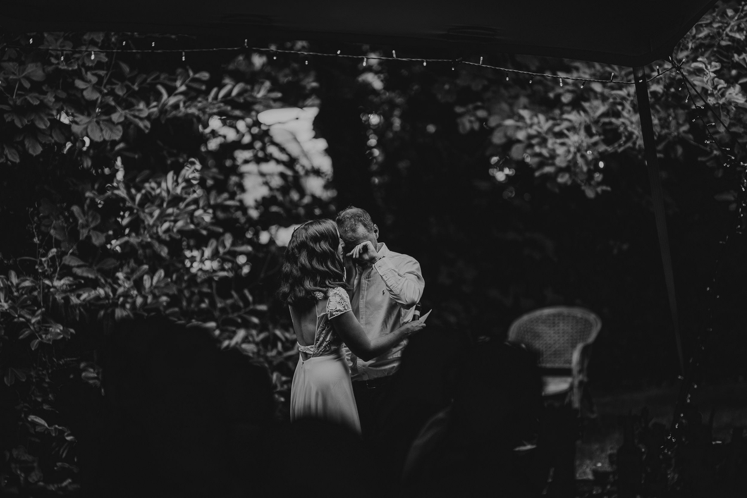 A couple dances under a canopy surrounded by trees and dim lighting.