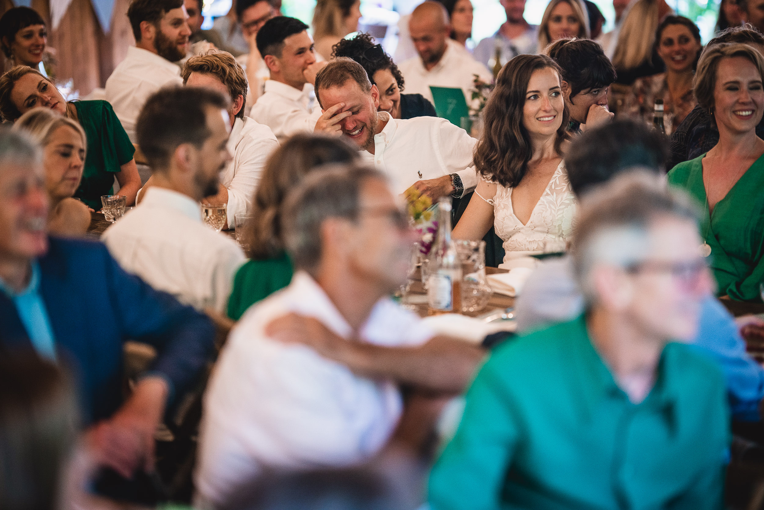 A group of people seated at tables, some smiling and others talking, in a lively indoor gathering.