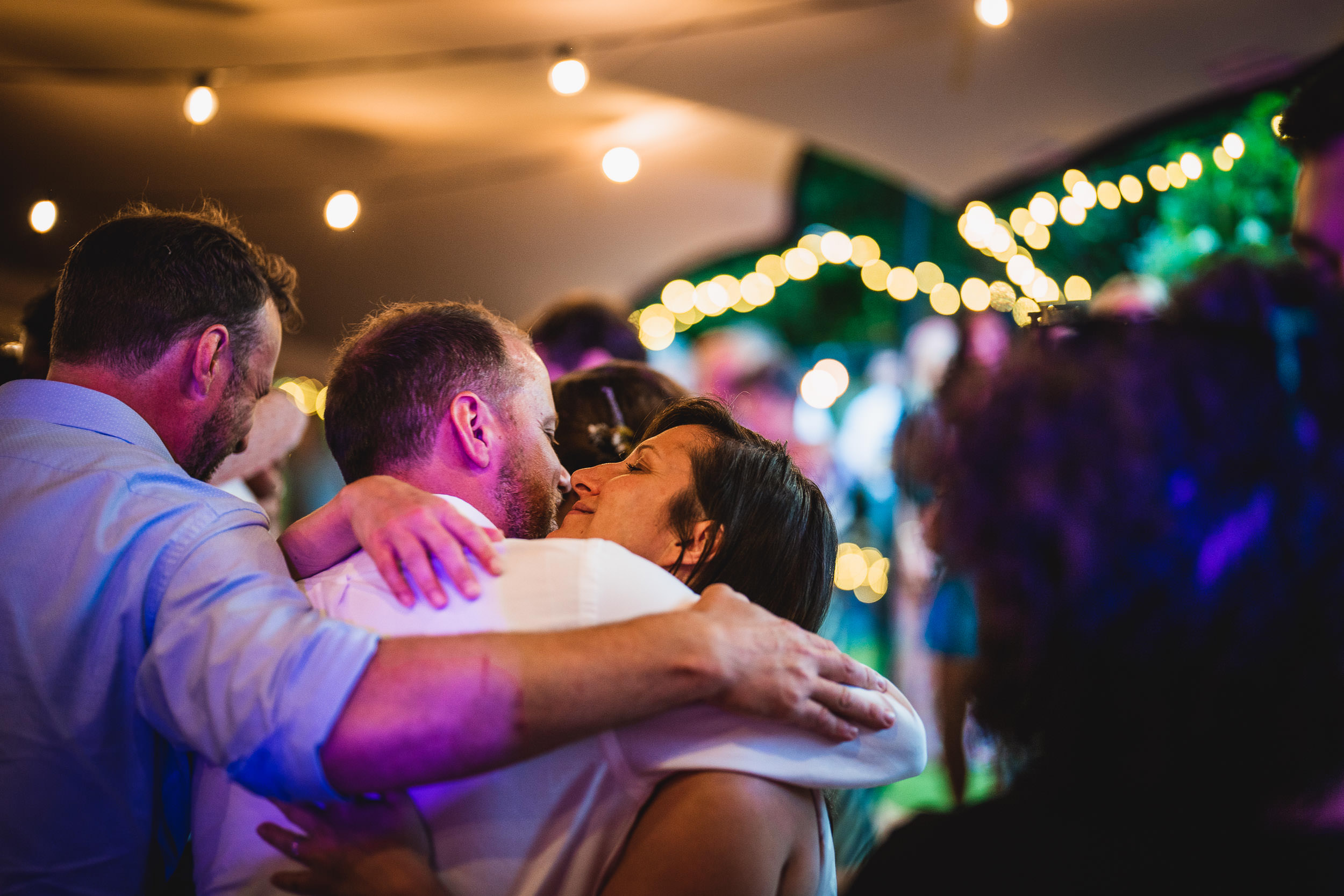 Group of people embracing at an outdoor event, with string lights in the background.