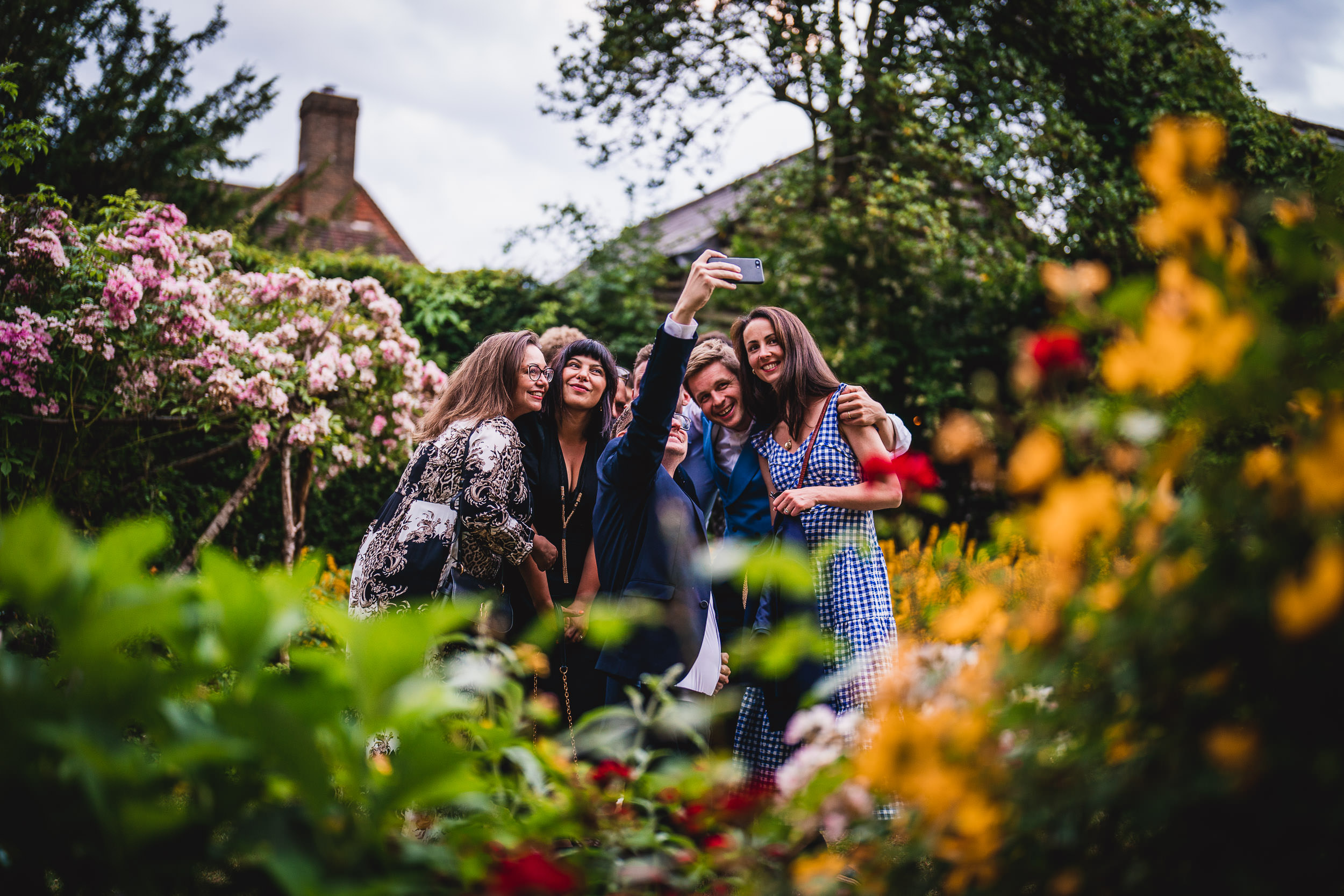 Four people taking a selfie together in a colorful garden with blooming flowers and trees in the background.