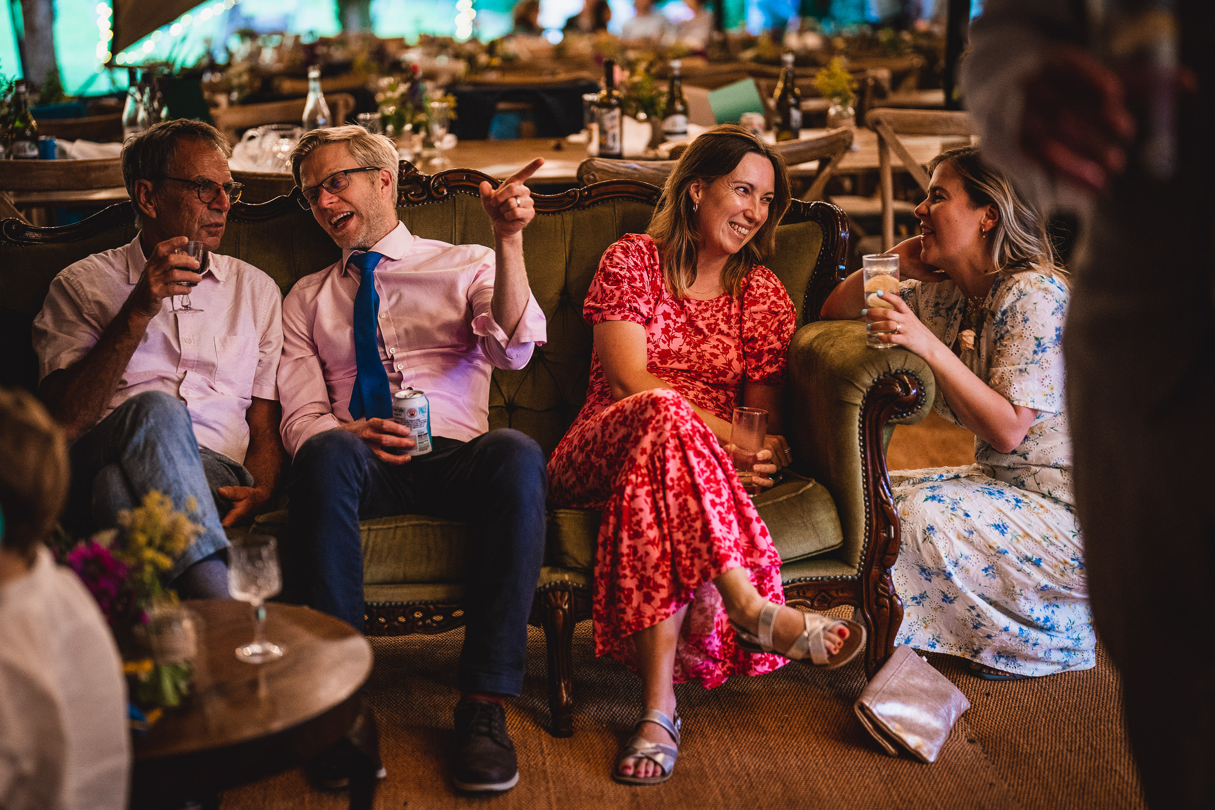 Four people are sitting on a couch, drinking and talking in a warmly lit setting.