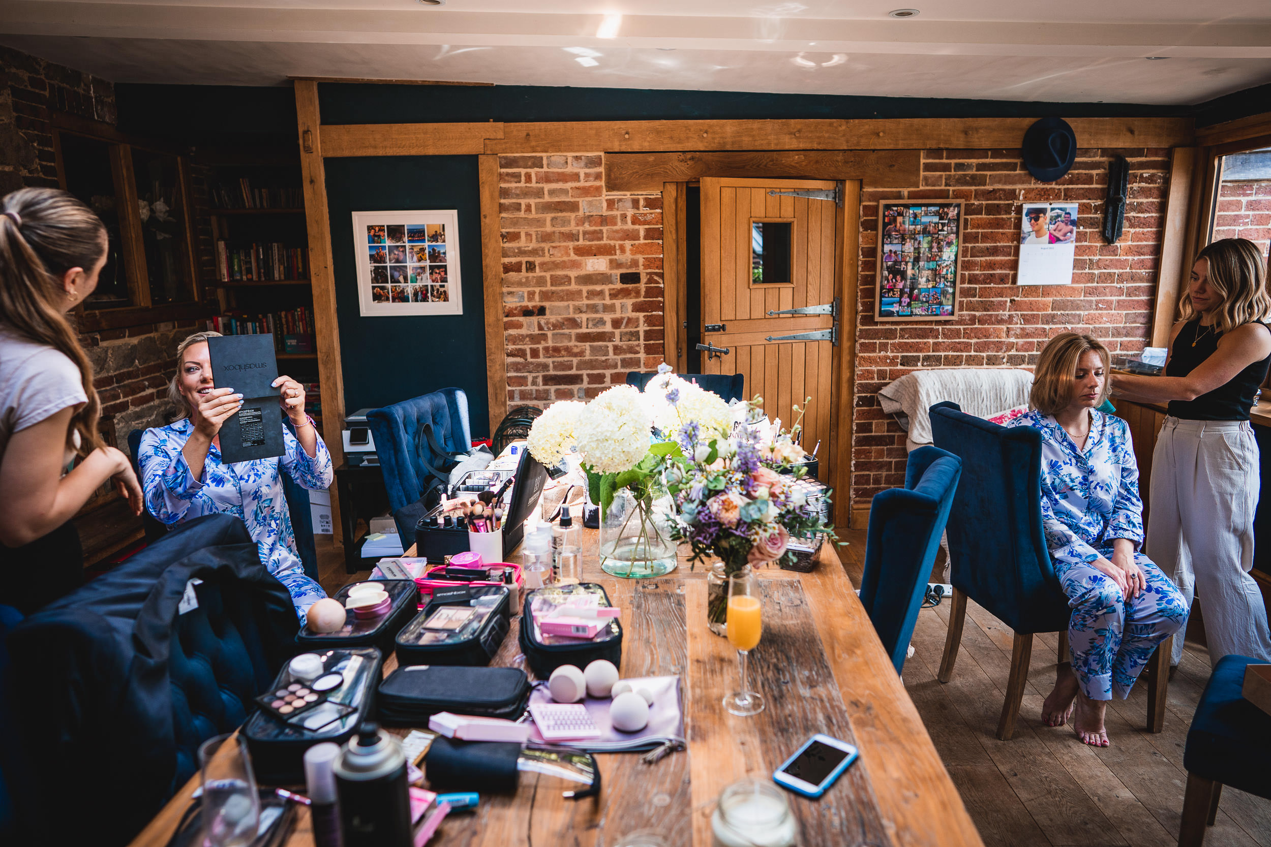 People getting ready in a room with beauty products on a table, flowers, and photographs on the walls.