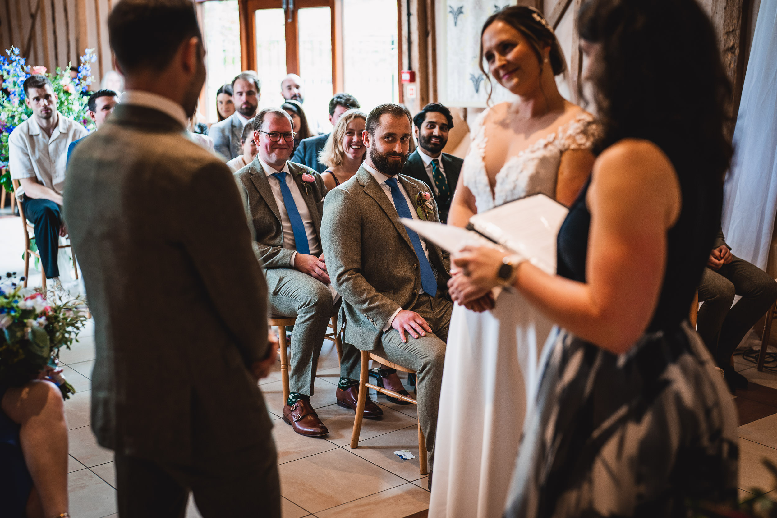 A couple stands in front of an officiant during a wedding ceremony. Guests are seated nearby, watching attentively.