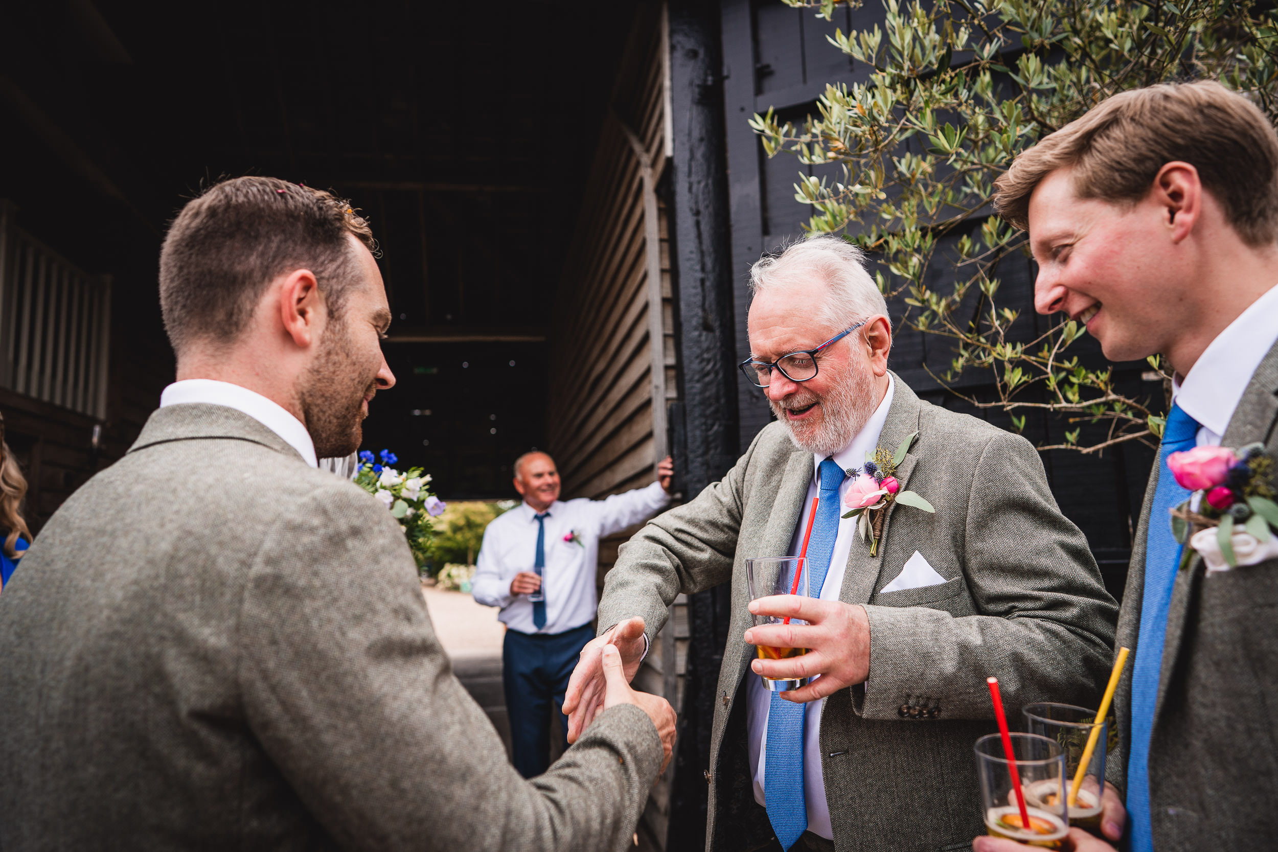 A group of men in suits shake hands and hold drinks outside a building during a festive gathering.