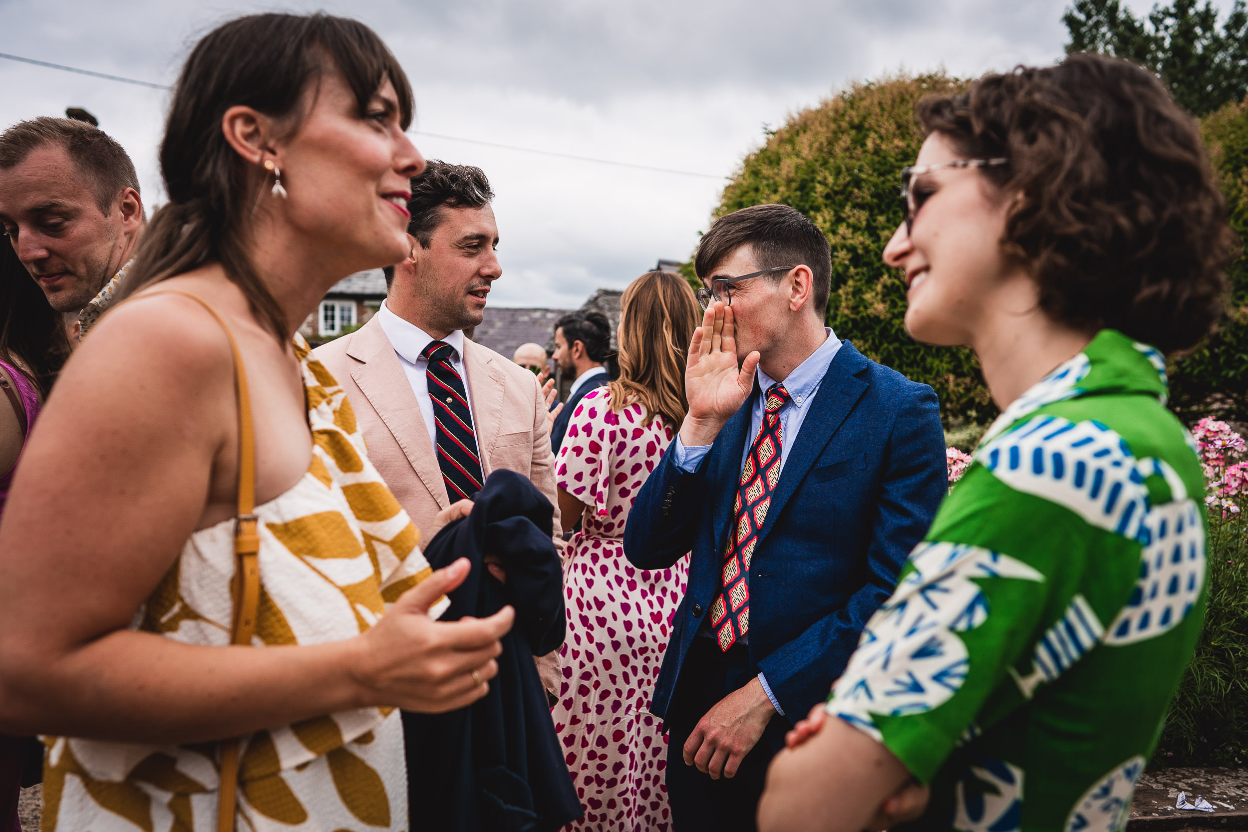 A group of people in colorful attire are conversing and smiling outdoors on a cloudy day.