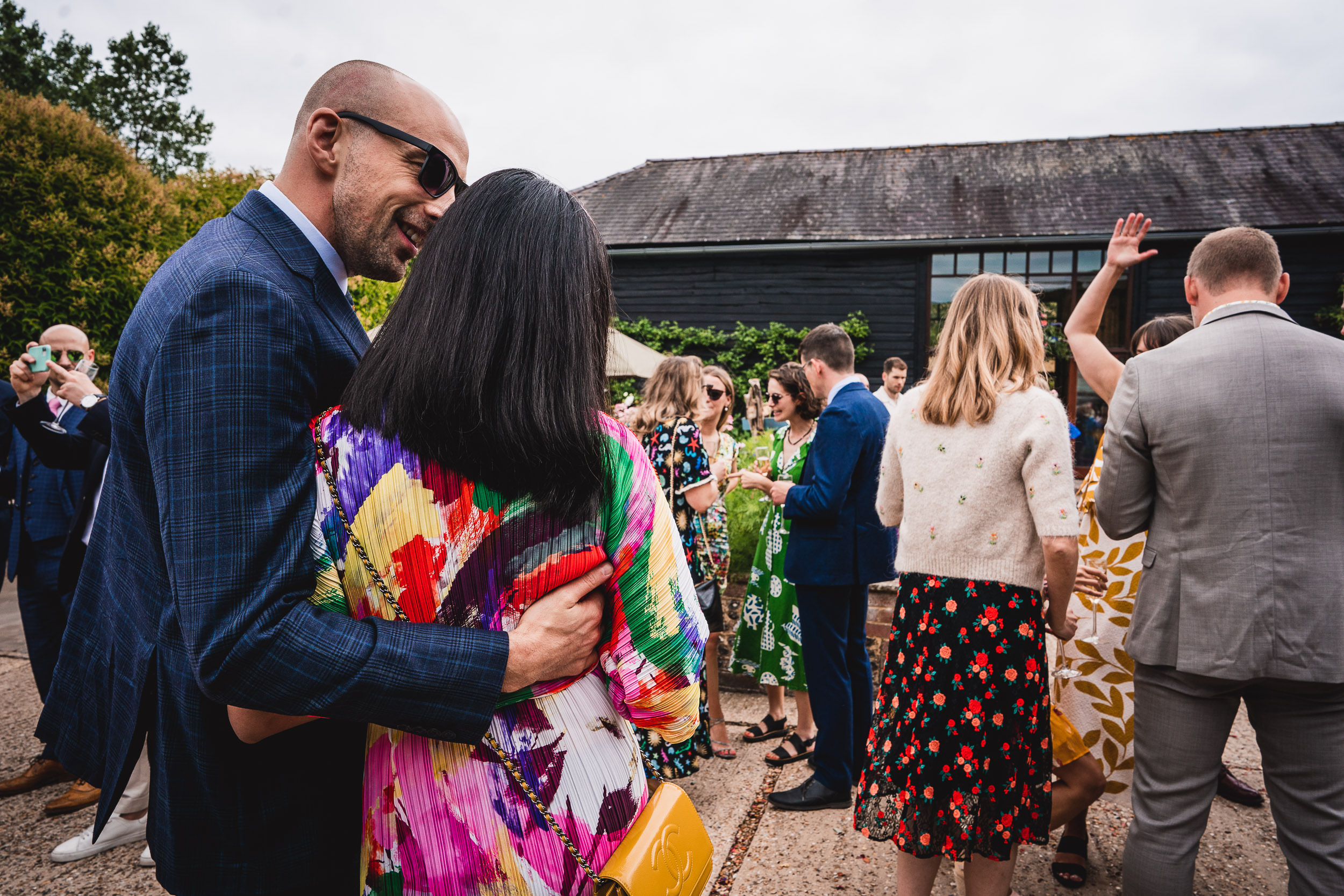 A group of people, dressed in colorful outfits, gather outdoors at an event. A man in sunglasses has his arm around a woman.