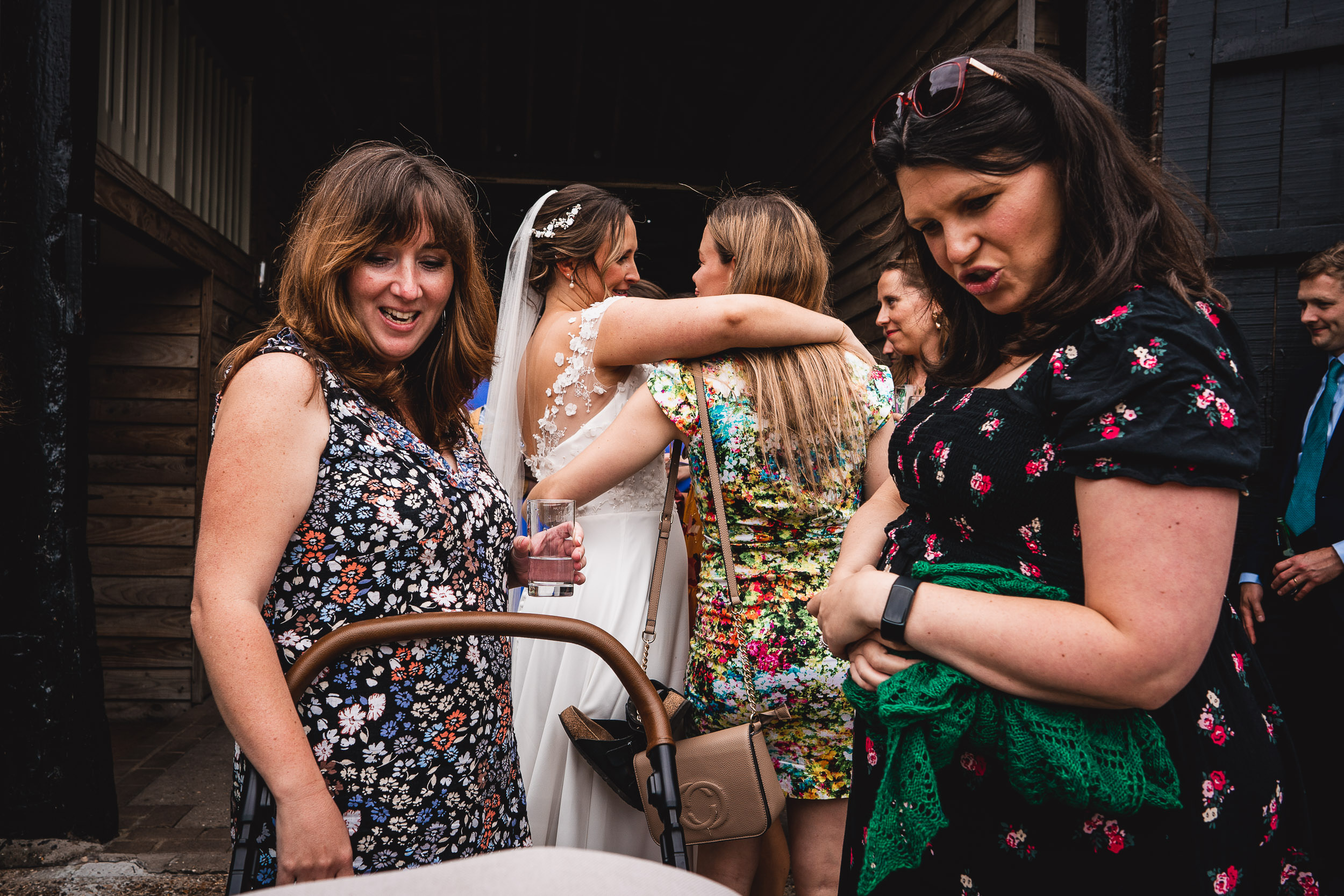 A group of people at an event, with one person holding a baby stroller, another sipping a drink, and two people hugging.