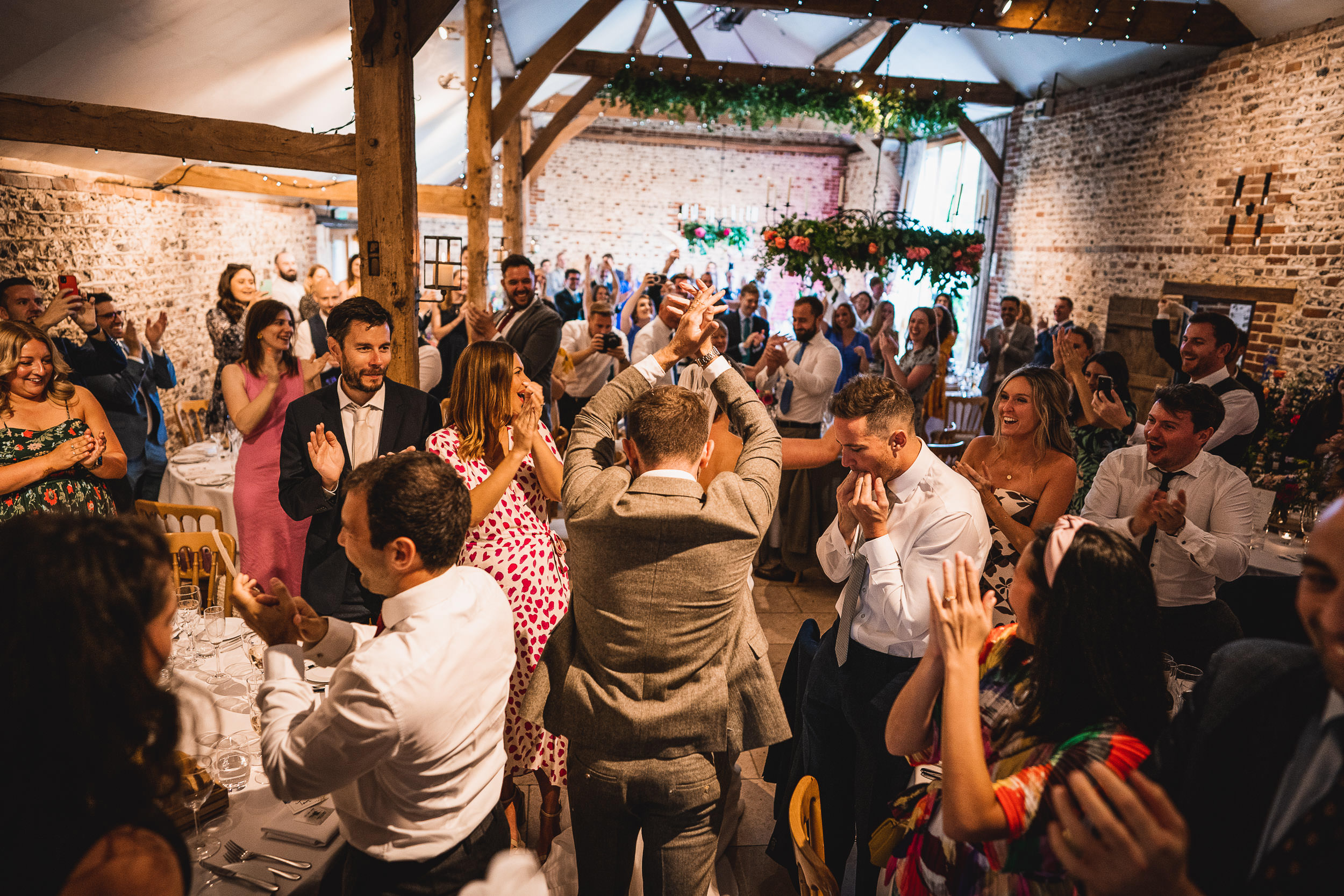 A group of people applauding a man at a rustic indoor event with wooden beams and brick walls.