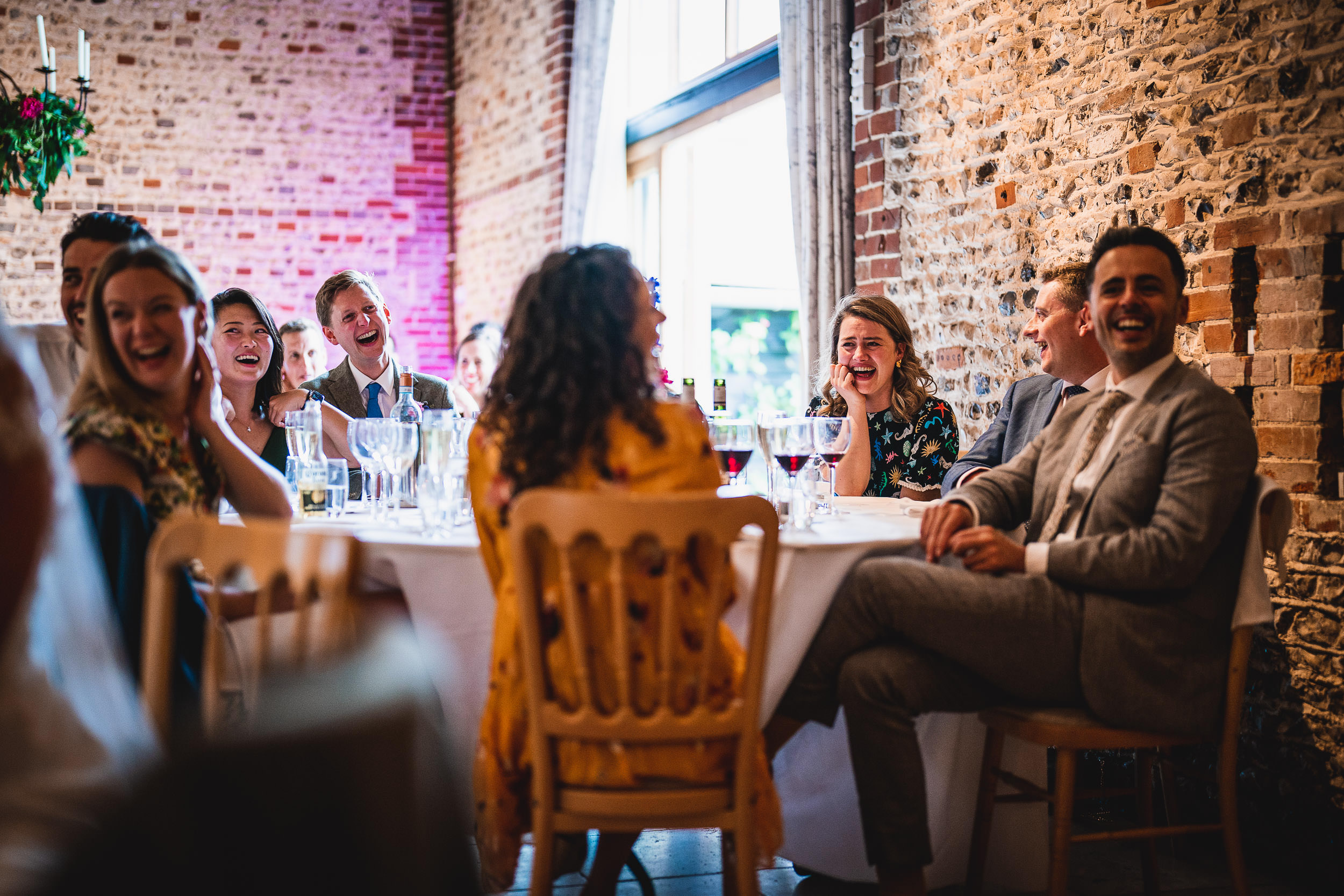 People seated around a table in a brick-walled room, laughing and smiling during what appears to be a social event or gathering.