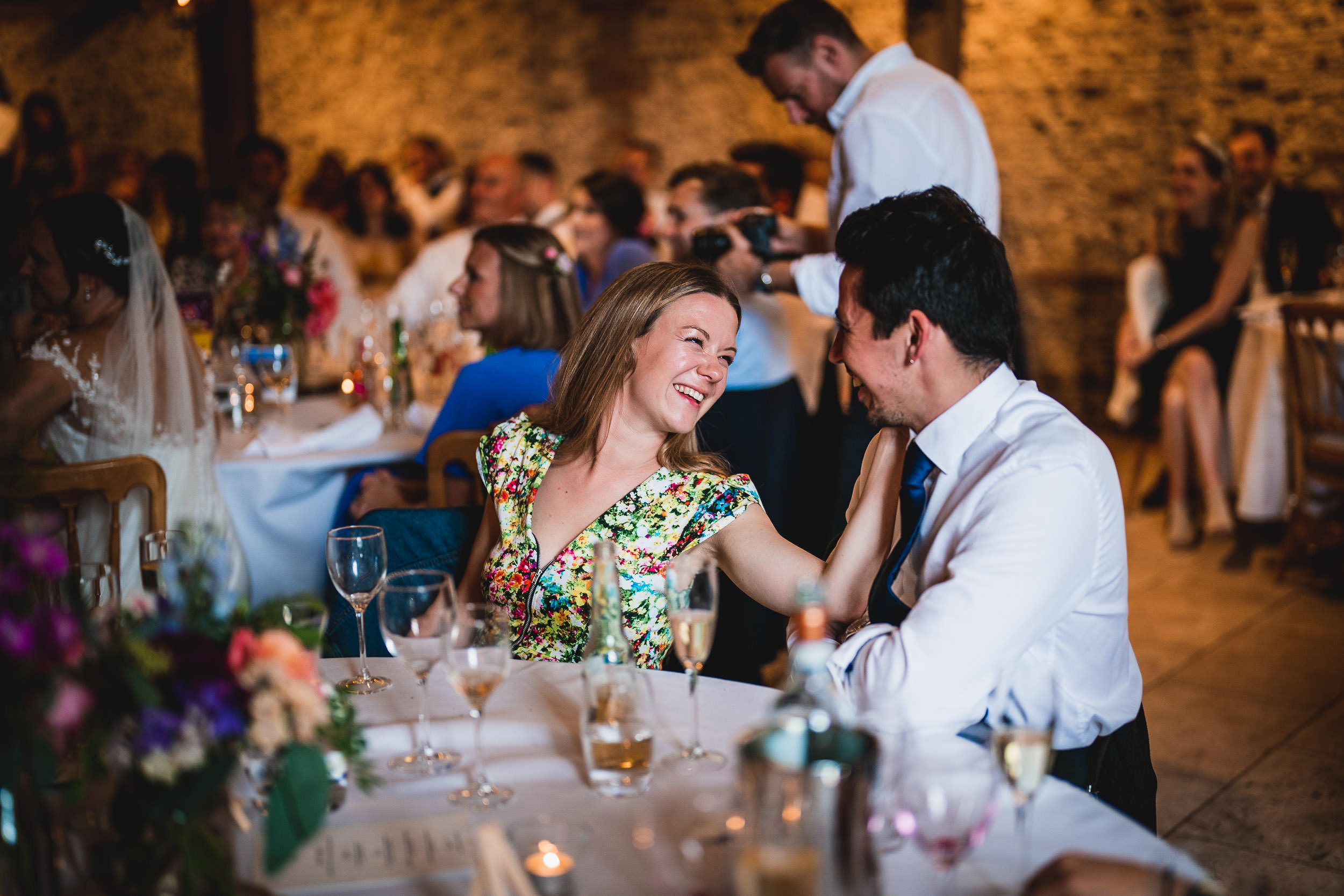 A woman and a man share a joyful moment while seated at a decorated table in a lively dining setting, surrounded by other guests.