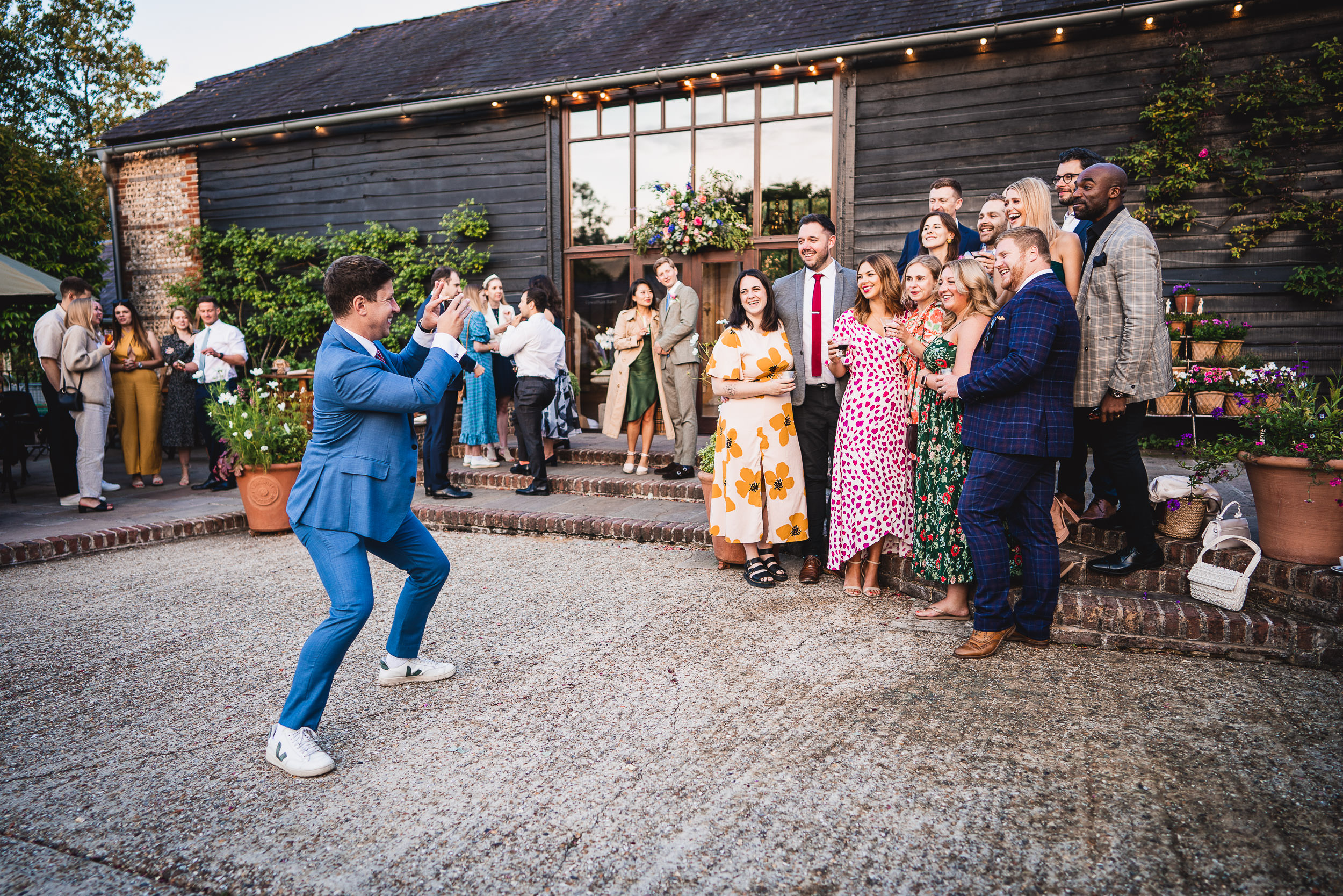 A group of people posing for a photo in front of a barn while a person in a blue suit takes the picture. The scene is outdoors with casual and colorful attire.