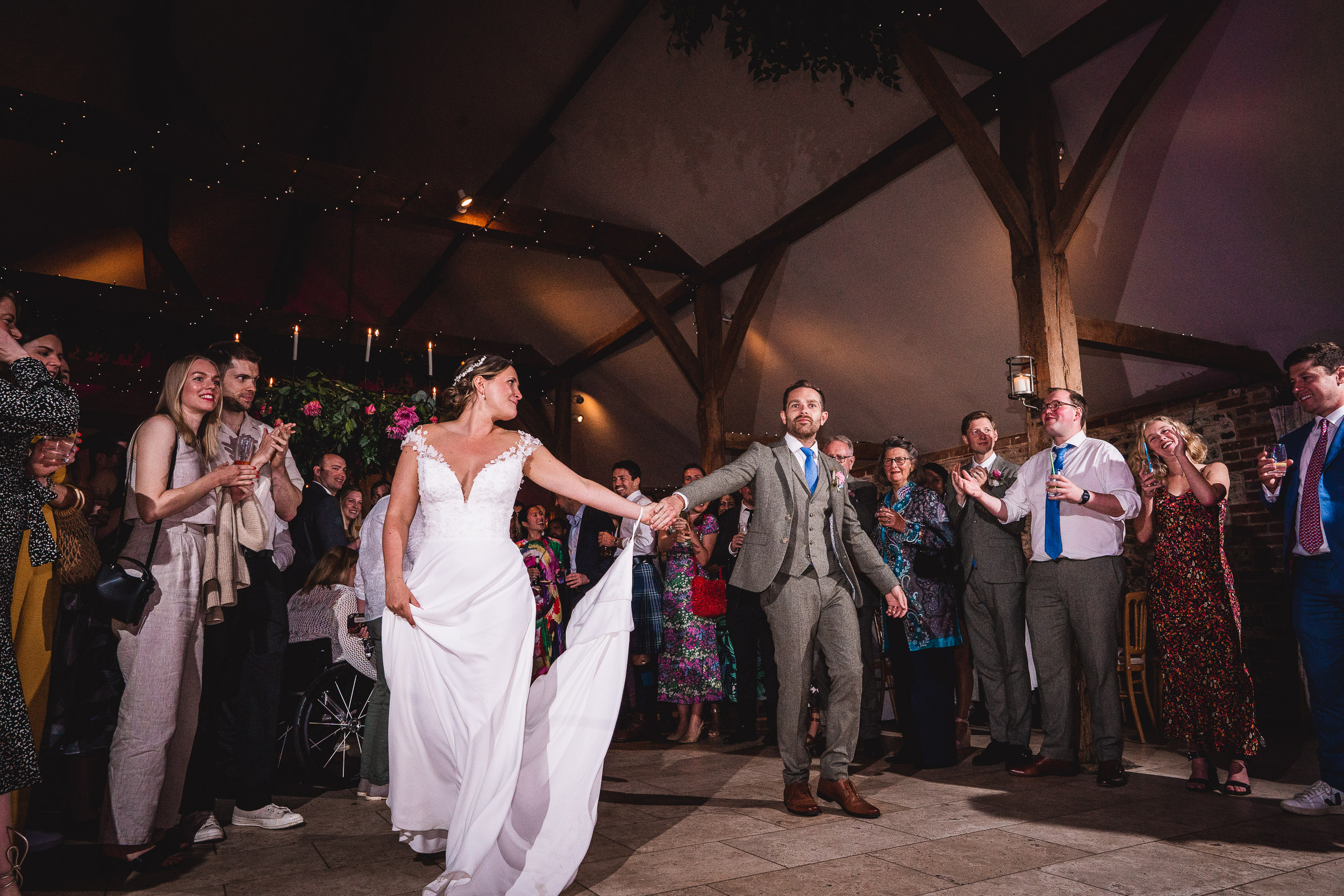 A bride and groom dance together in a rustic venue, surrounded by applauding guests.