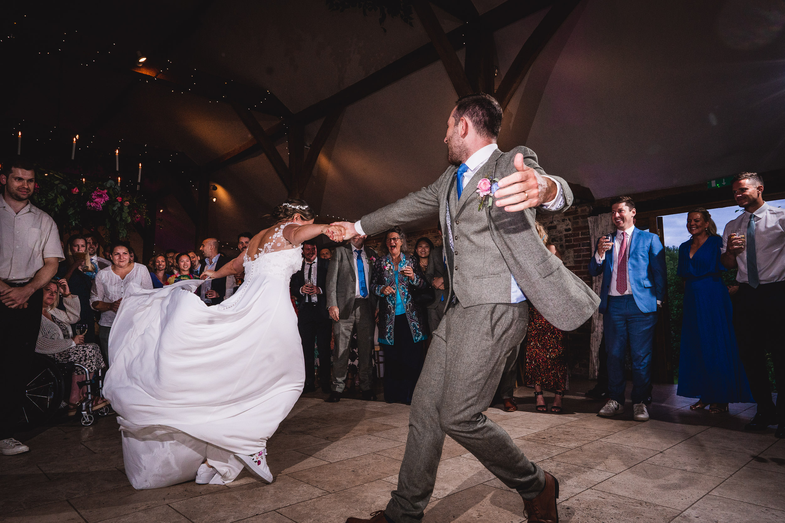 A bride and groom dance energetically at their wedding, surrounded by applauding guests in a reception hall.