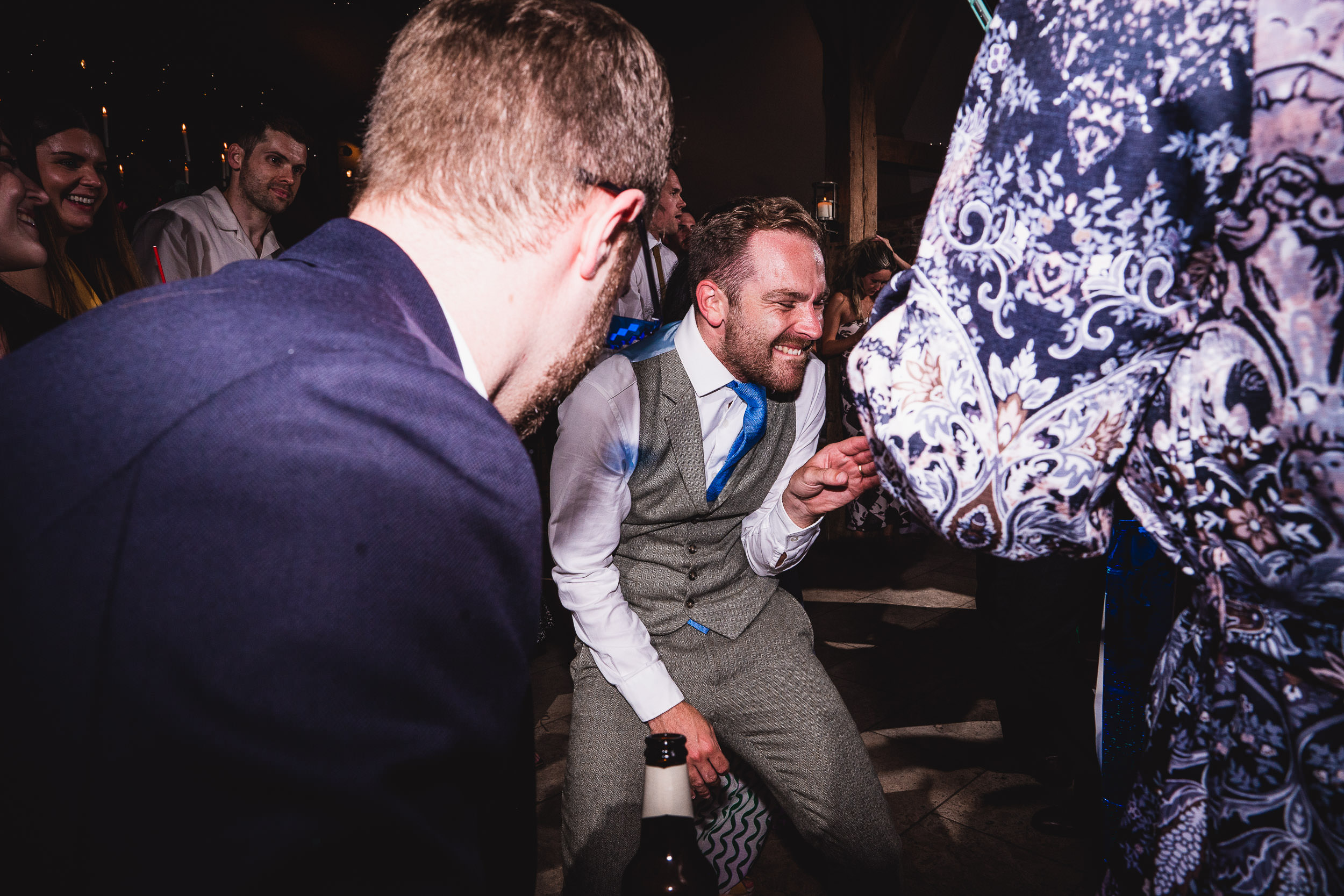 A man in a suit dances energetically at a party, surrounded by other people.